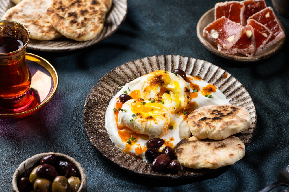 Authentic Turkish breakfast with poached eggs, olives, flatbread, and tea.