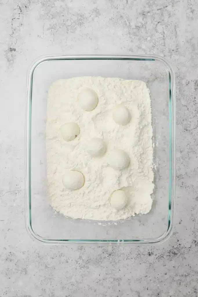 Fried-goat-cheese-balls-3-1 - Step-by-Step Guide to Perfect Fried Goat Cheese Balls Glass tray with dough balls in flour on a gray textured surface.
