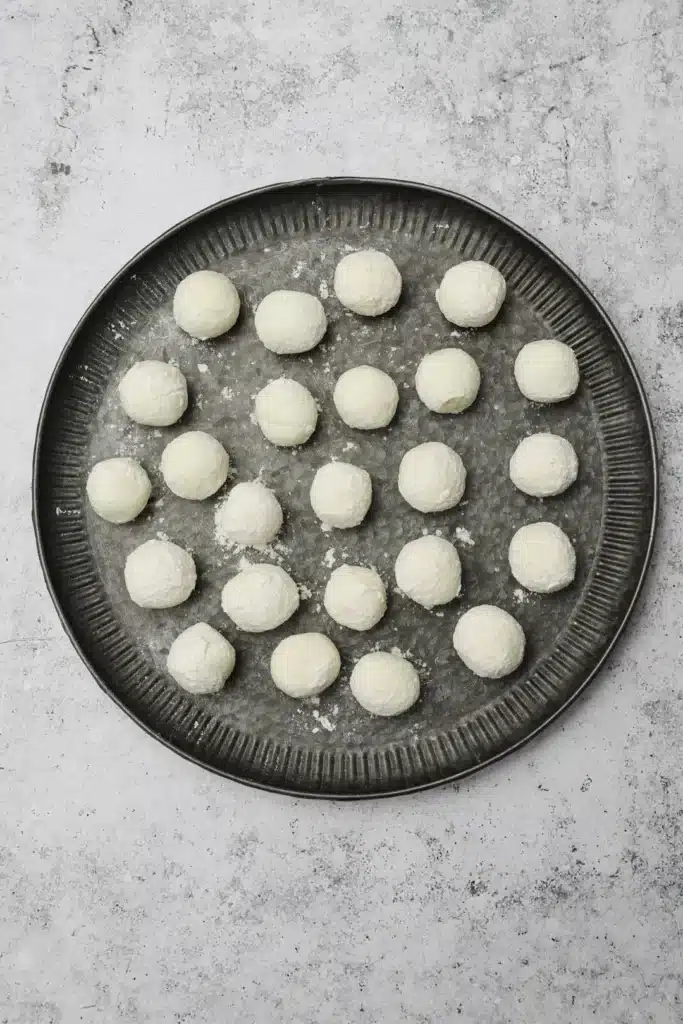 Fried-goat-cheese-balls-4-1 - Step-by-Step Guide to Perfect Fried Goat Cheese Balls Round dough balls on a dark baking tray ready for baking, placed on a textured light surface.