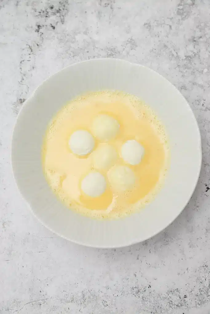 Fried-goat-cheese-balls-5 - Step-by-Step Guide to Perfect Fried Goat Cheese Balls White dumplings in creamy yellow soup in a textured white bowl on a gray surface.