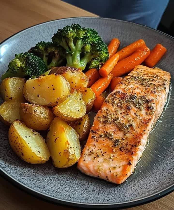 Grilled salmon with roasted potatoes, carrots, and broccoli on a dark plate – a delicious healthy meal.