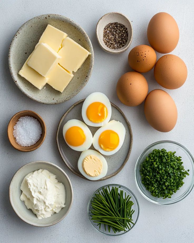 Ingredients for egg salad: butter, eggs, salt, pepper, mayonnaise, chives on a light background.