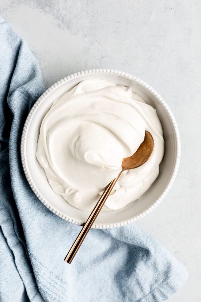 Creamy yogurt in a bowl with a spoon, placed on a blue cloth; perfect for healthy breakfast ideas.