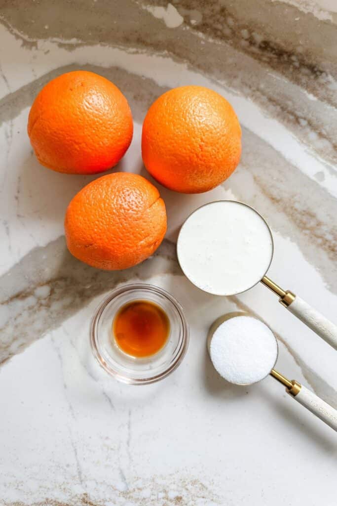 Fresh oranges, flour, sugar, and vanilla extract on a marble countertop. Perfect ingredients for baking.
