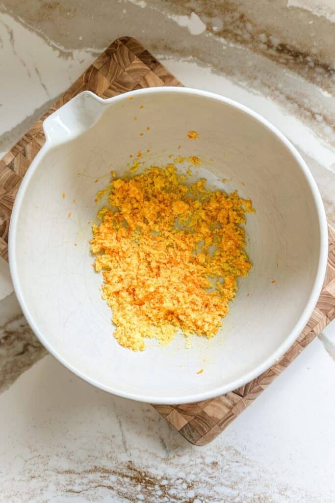 Bowl with orange zest and sugar mix on a wooden board, ideal for enhancing citrus dessert recipes.