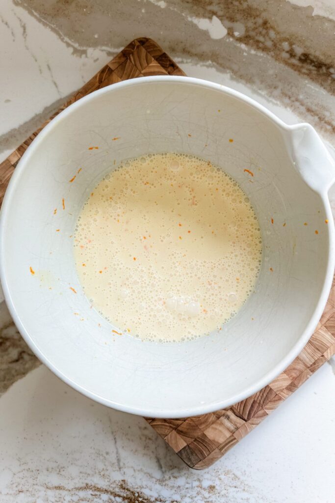 Batter in a white mixing bowl on a wooden board, ready for cooking or baking preparation.