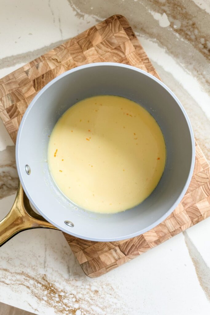 Creamy yellow sauce in a pot on a wooden cutting board, ready for cooking.