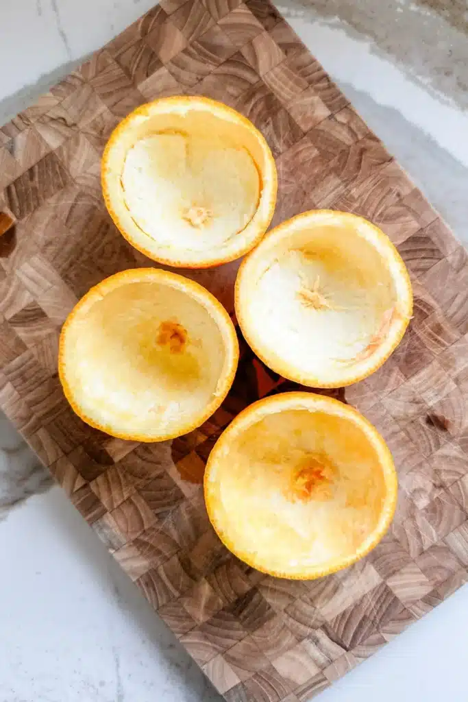 Four empty orange halves on a wooden cutting board, ready for creative culinary use or decoration ideas.