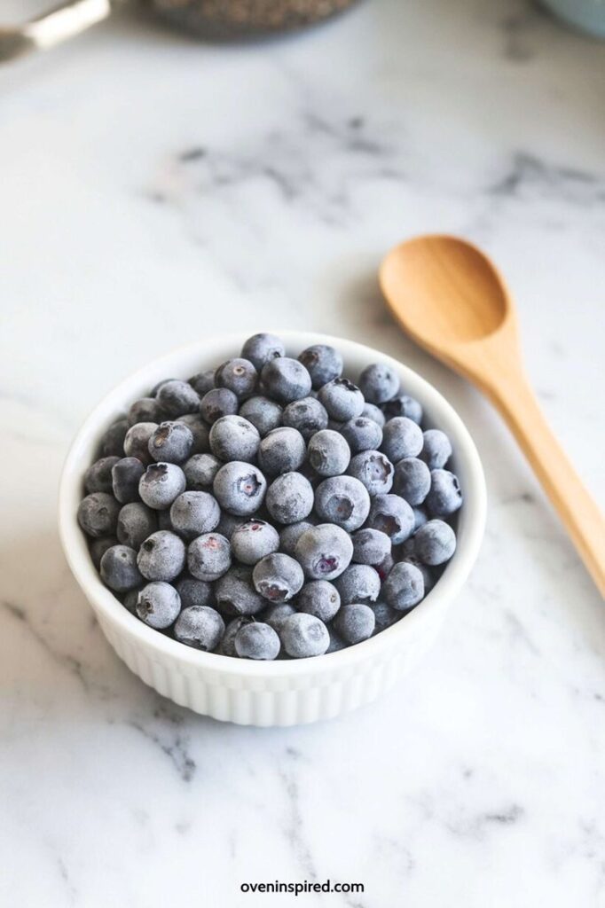 Bowl of fresh blueberries on marble countertop with a wooden spoon. Perfect for healthy snacks or recipes.