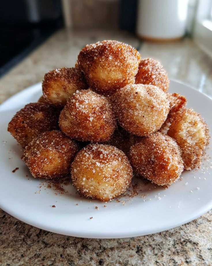 A plate of freshly baked, sugar-coated donut holes stacked on a kitchen counter.