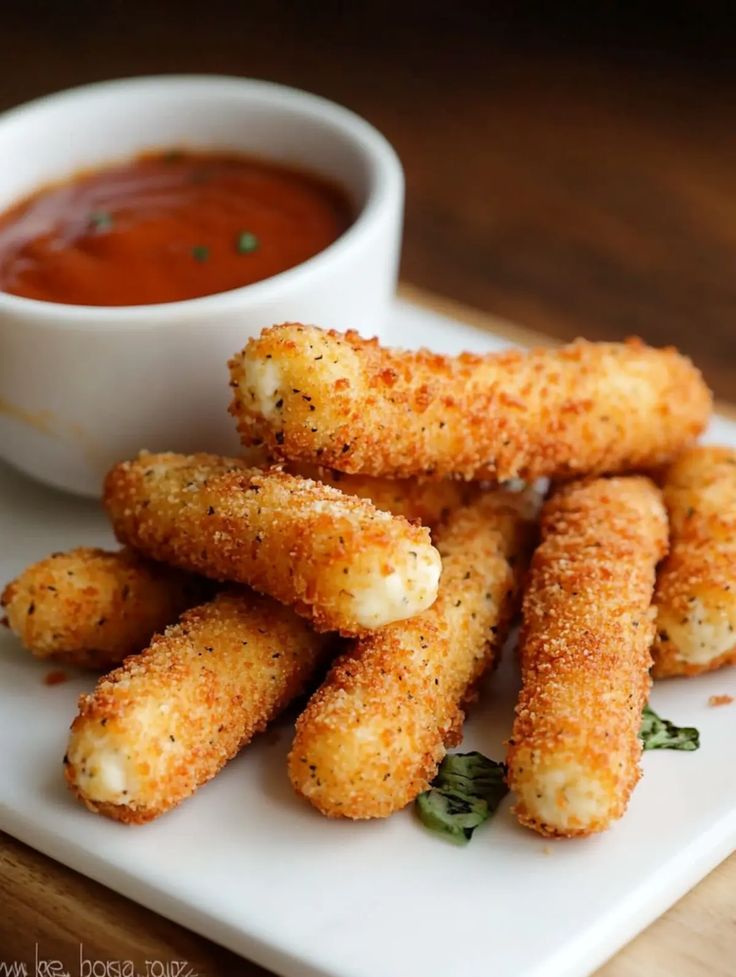 Crispy mozzarella sticks with marinara sauce on a white plate, perfect for a cheesy appetizer or snack.