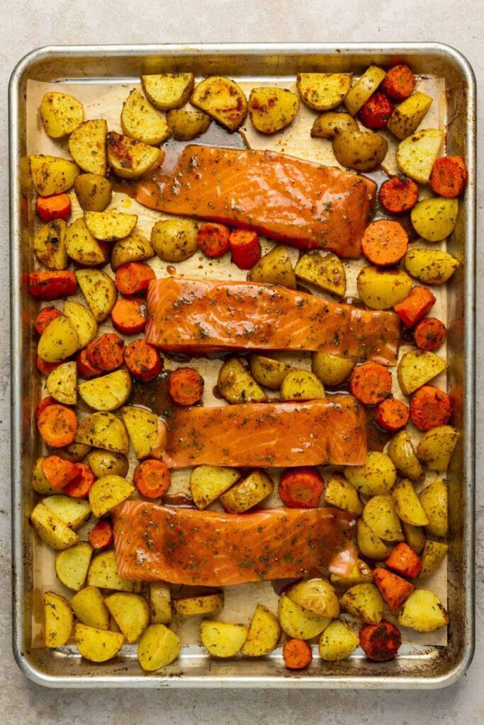 Baked salmon with roasted potatoes and carrots on a tray, seasoned for a healthy, delicious meal.