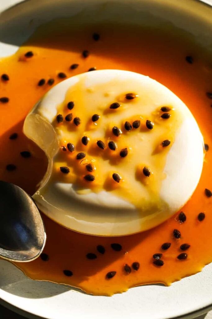 Passion Fruit Panna Cotta - Silky, Tropical Coconut & Passion Fruit Panna Cotta Creamy panna cotta topped with vibrant passion fruit sauce on a white plate, served with a spoon. Coconut & Passion Fruit Panna Cotta