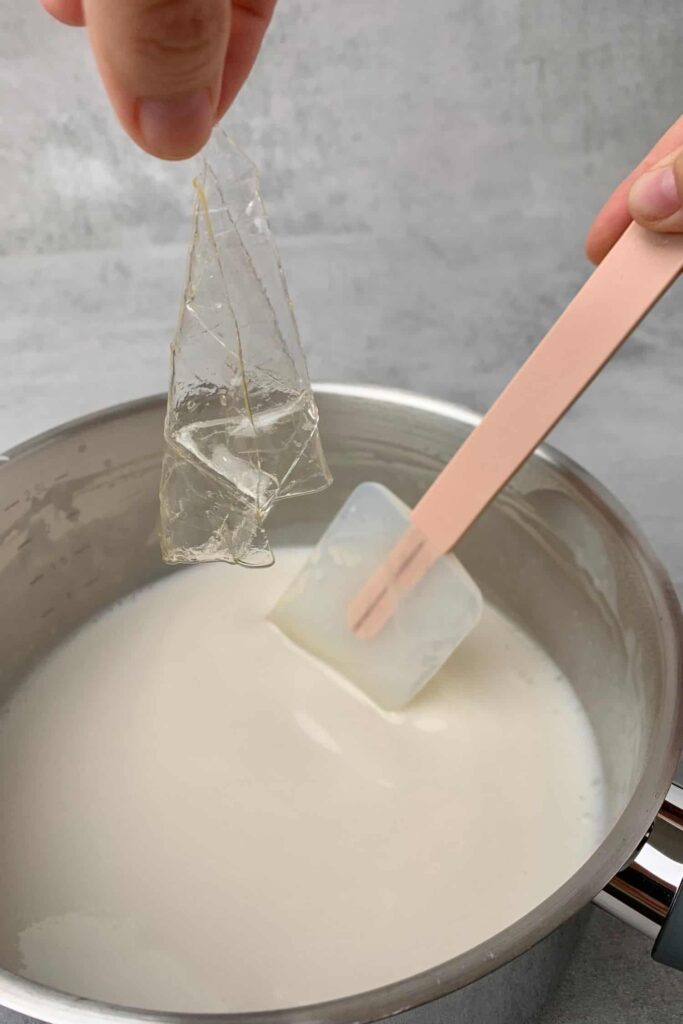 Passion-fruit-panna-cotta - Silky, Tropical Coconut & Passion Fruit Panna Cotta Adding gelatin sheet to saucepan with milk, stirring with pink spatula.