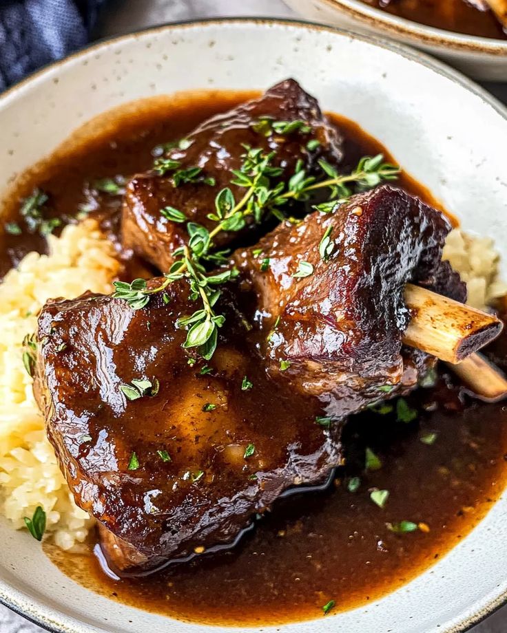 Tender braised beef short ribs in rich sauce, garnished with fresh herbs, served over creamy mashed potatoes.