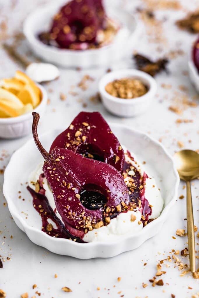 Red Wine Poached Pears - Elegant Winter Dessert: Perfect Mulled Wine Poached Pears Elegant red wine poached pears on whipped cream, topped with crushed nuts, served on a white plate.