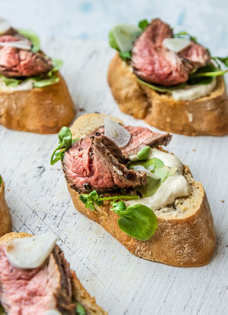 Rustic open-faced sandwiches with sliced roast beef, creamy sauce, and fresh greens on wooden table.