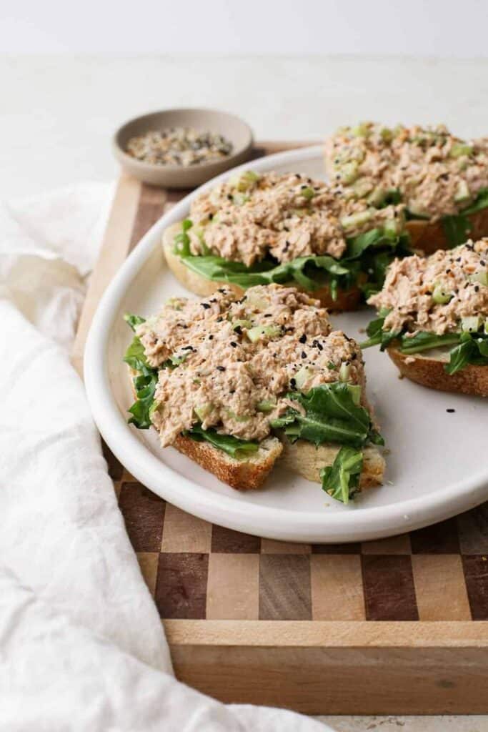Open-faced tuna salad sandwiches topped with greens and seeds on a white plate, ready to serve.
