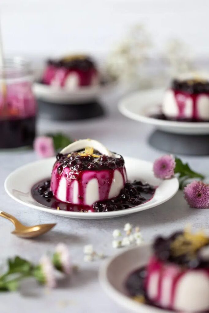 Creamy panna cotta topped with vibrant berry sauce, garnished with lemon zest on a white plate.