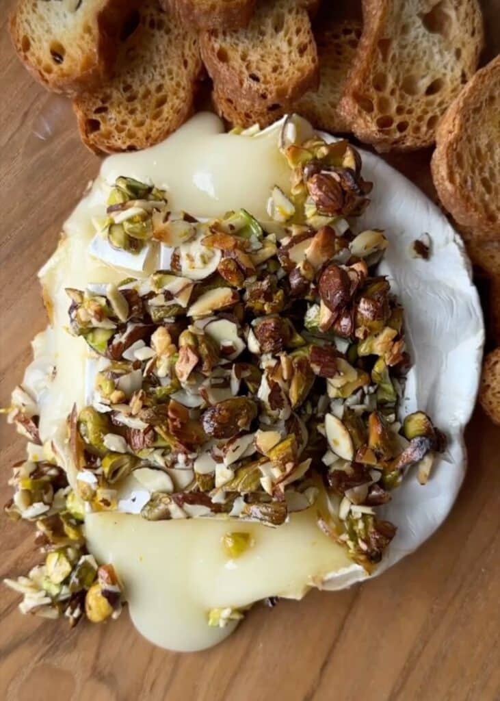 Warm Brie with pistachios posted by anthroliving - Melted Brie with Honey & Pistachios in 20 Minutes Melted brie topped with nuts and served with toasted bread slices on a wooden board.