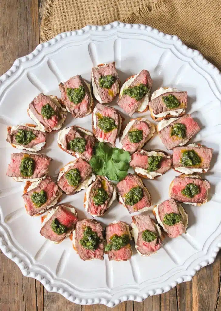 Sliced steak appetizers with pesto on a white plate, perfect for gatherings and parties.
