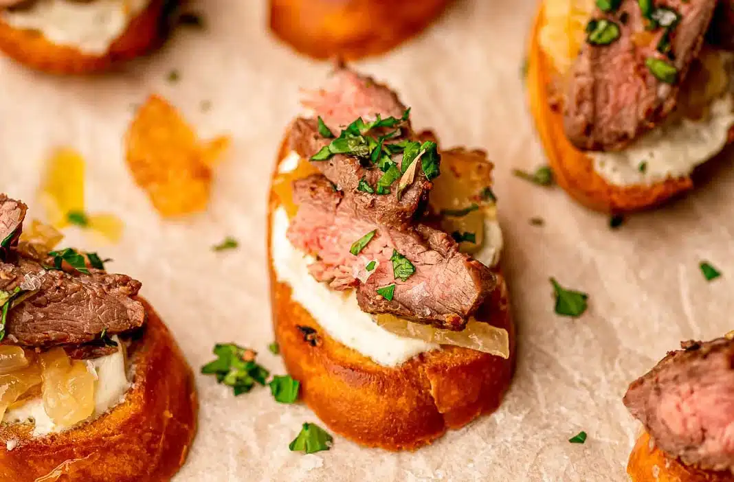 Sliced steak on crostini with creamy cheese and fresh herbs, perfect appetizer for parties or gatherings.