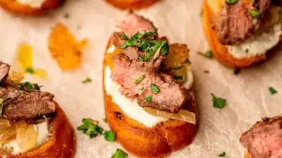 Sliced steak on crostini with creamy cheese and fresh herbs, perfect appetizer for parties or gatherings.
